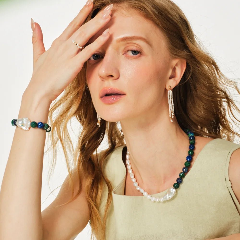 Soft close-up of woman’s face with pulled-back hair, layering mixed turquoise baroque pearl silver necklace and bracelet against muted dark neutral backdrop