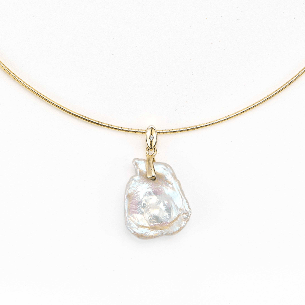 Close-up of iridescent baroque pearl pendant on gold snake chain