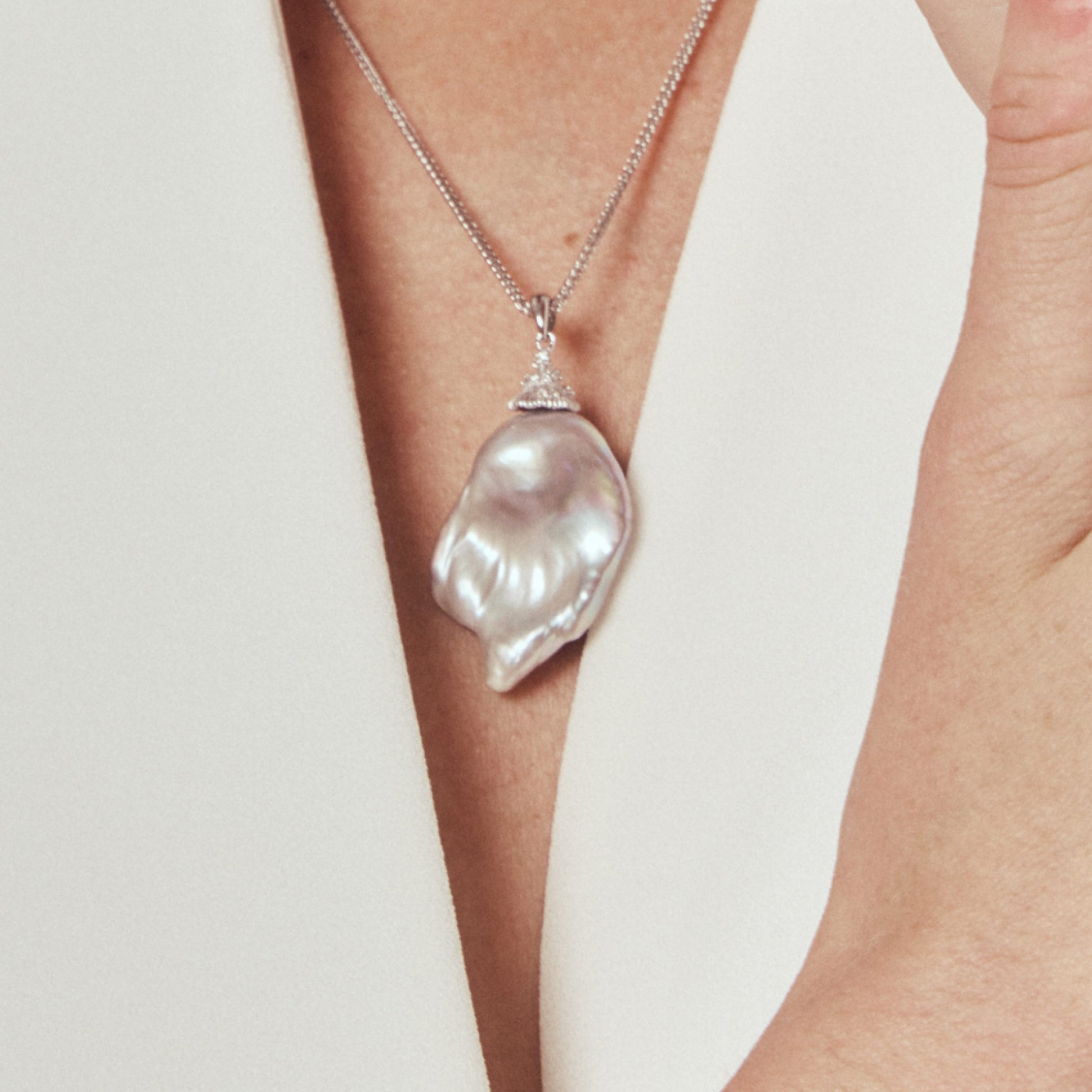 Model wearing gray pearl pendant with white blazer