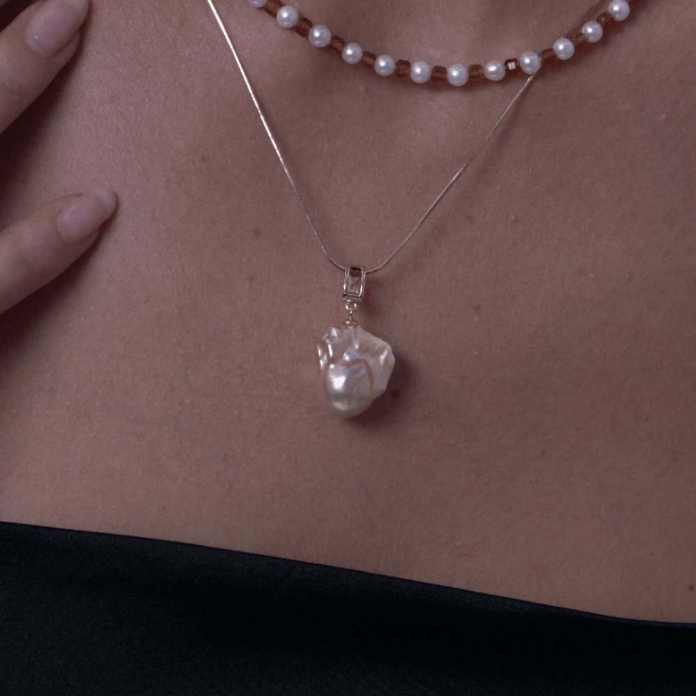 Close-up of pink luster baroque pearl pendant on gold chain on model