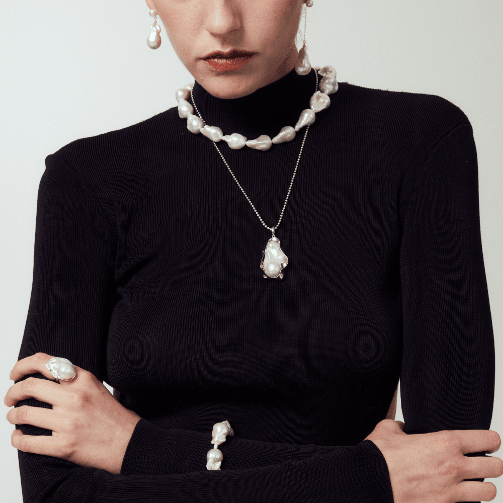Detailed view of a model wearing a large natural pearl necklace with silver baroque accents and organic textures.