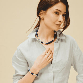 female model in light linen collared shirt, wearing lapis baroque pearl necklace, matching bracelet and pearl stacking ring against soft beige neutral backdrop