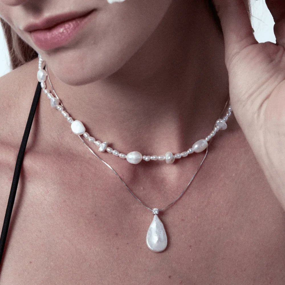 Soft close-up shot of female model’s collarbone wearing minimalist teardrop cubic zirconia baroque pearl silver pendant, neutral everyday gentle feminine styling
