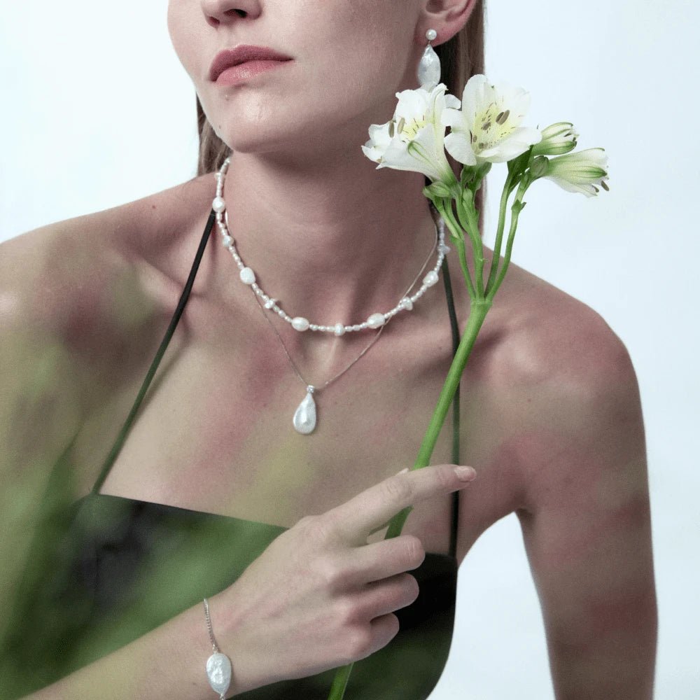 Medium bust shot of woman with white floral props layered with teardrop drop pearl silver pendant, soft minimalist bridal romantic aesthetic