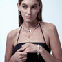 Medium bust shot of woman in minimalist black camisole, layering coin baroque pearl gold bracelet with matching pearl necklaces against soft warm neutral backdrop