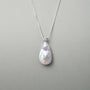 Neutral grey close-up capturing soft milky iridescent luster of teardrop baroque pearl and tiny star sparkle of top cubic zirconia silver setting
