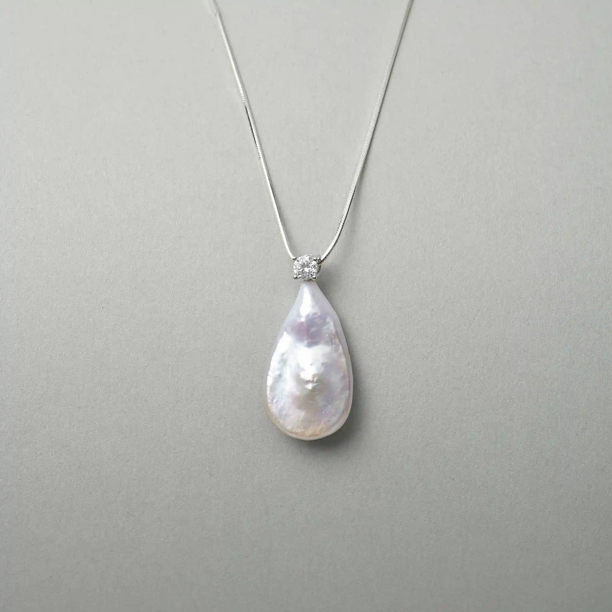 Neutral grey close-up capturing soft milky iridescent luster of teardrop baroque pearl and tiny star sparkle of top cubic zirconia silver setting

