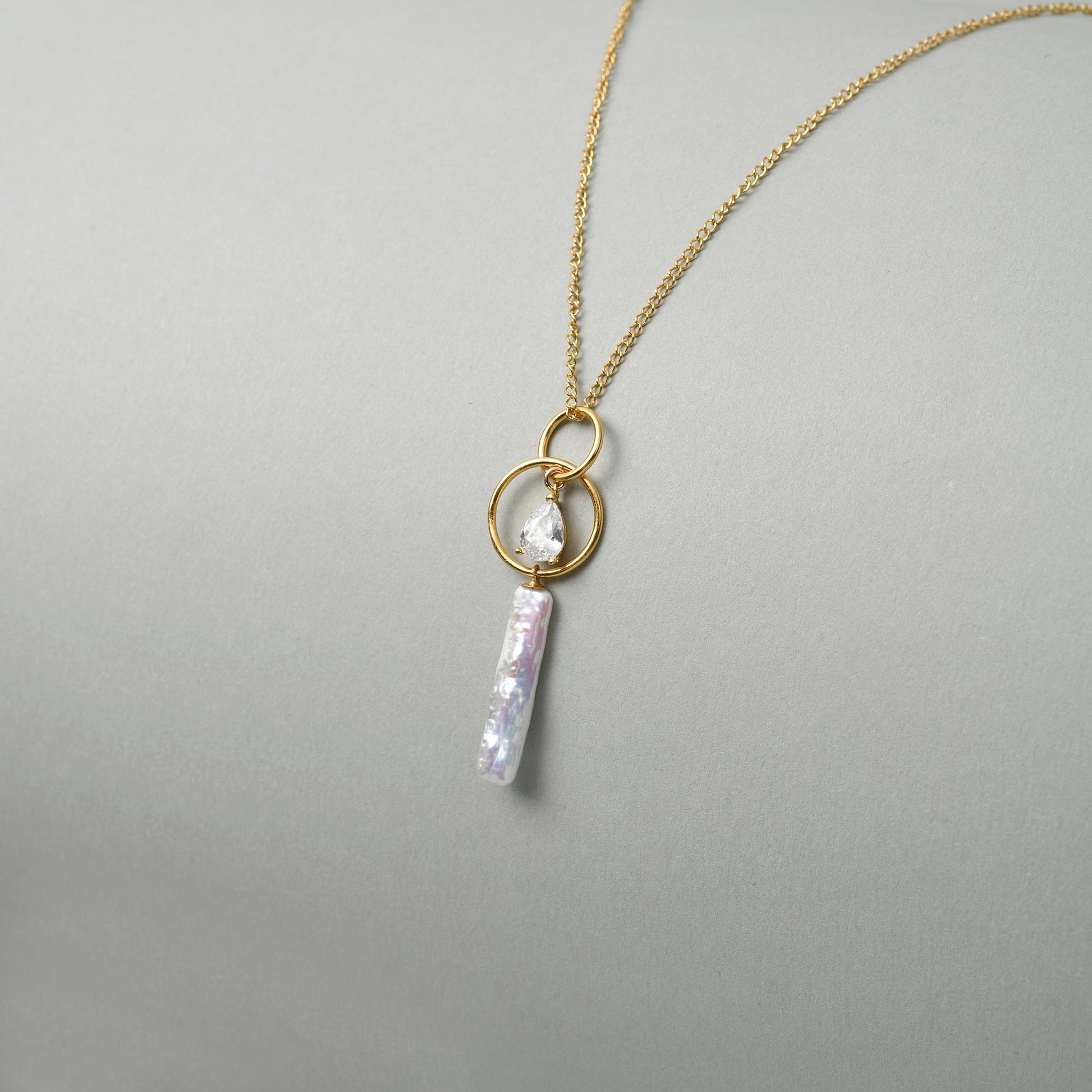 Side view of 18k gold orbit baroque pearl pendant on neutral background