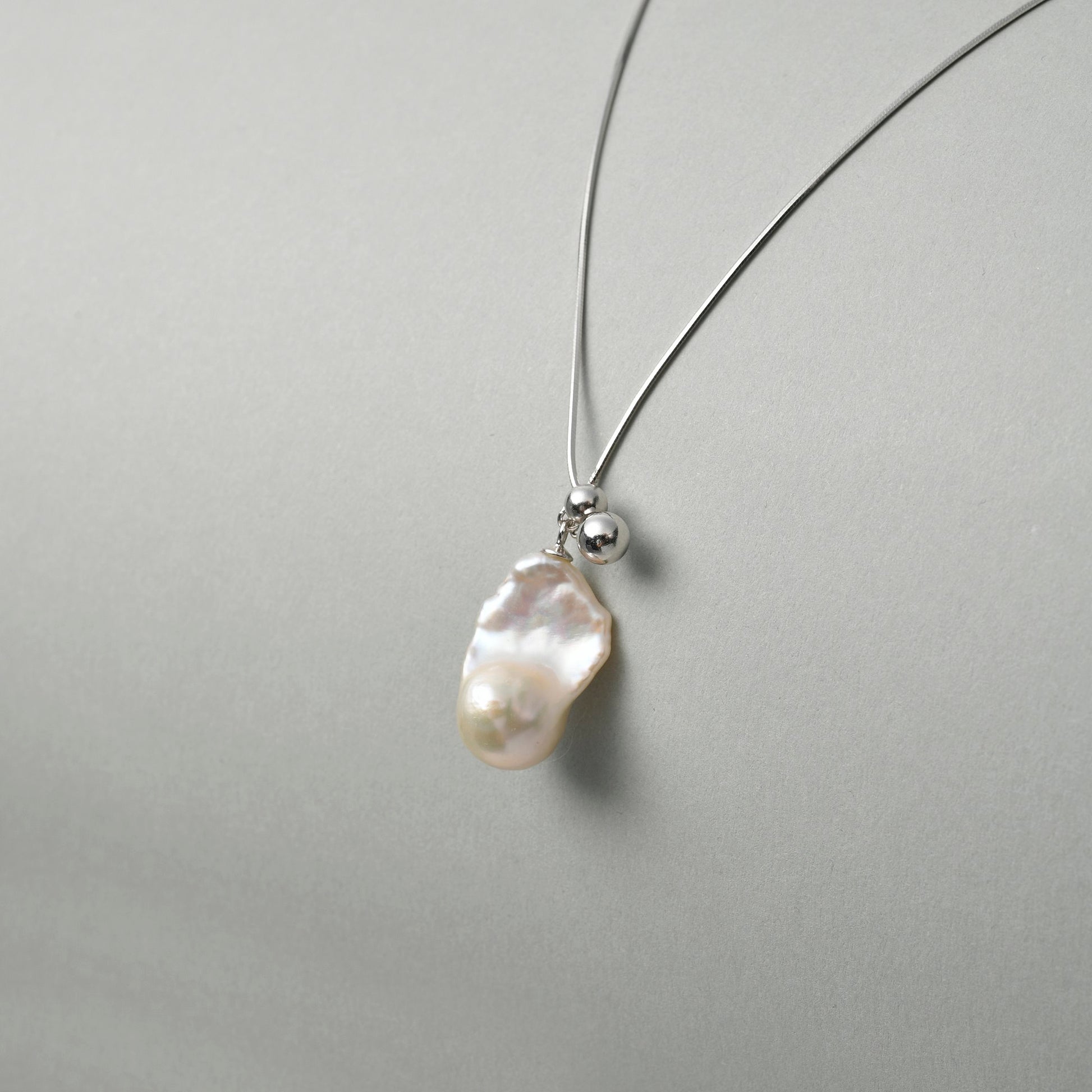 Side view of mini drop pearl pendant on neutral background