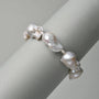 Close-up shot of sterling silver baroque pearl bracelet strung with oversized organic white pearls, draped over smooth light grey cylindrical display prop