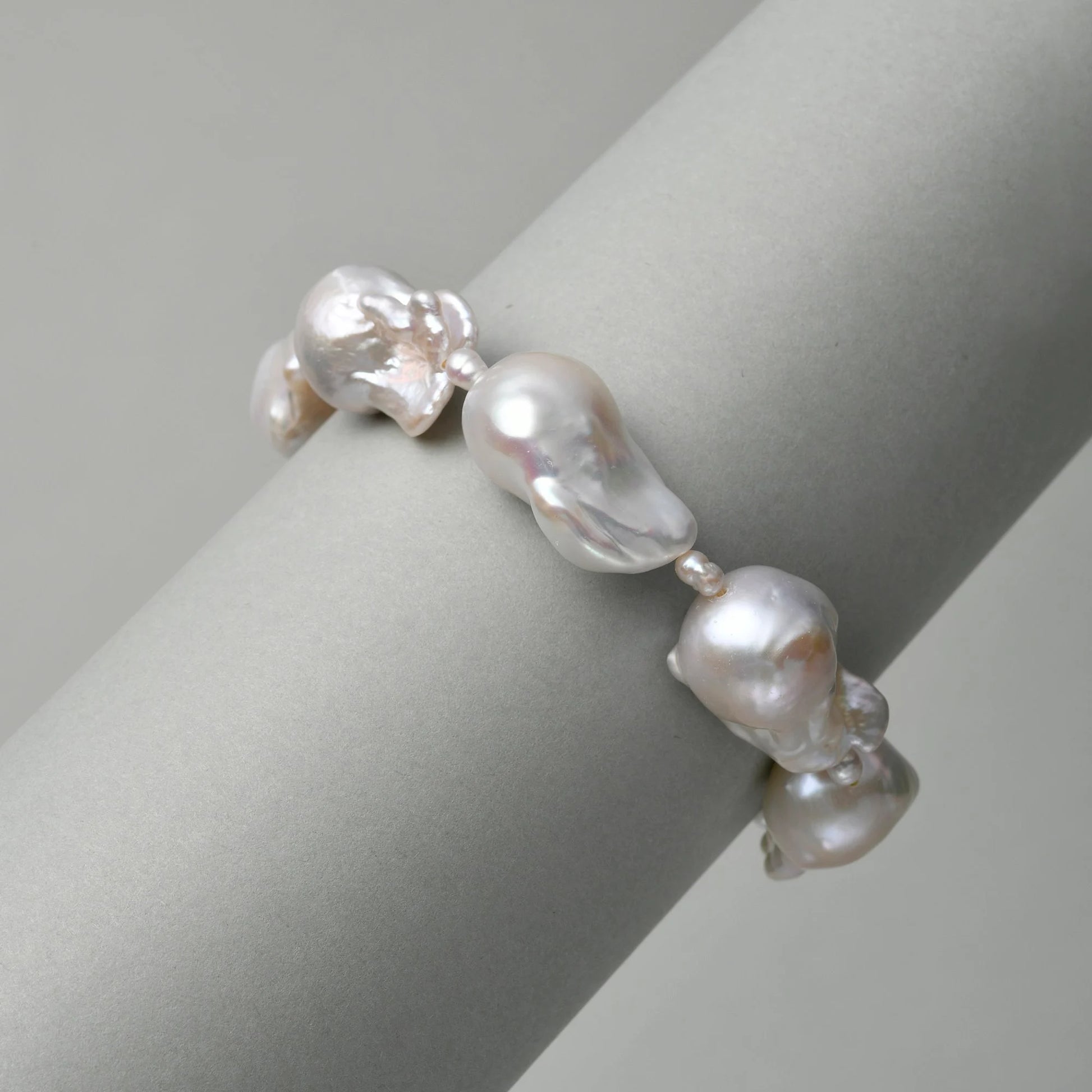 Close-up shot of sterling silver baroque pearl bracelet strung with oversized organic white pearls, draped over smooth light grey cylindrical display prop