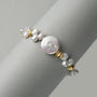 Top-down clean white close-up highlighting texture contrast between oversized luminous coin button baroque pearl, mini keshi pearls and sculptural twisted 18k gold metal beads