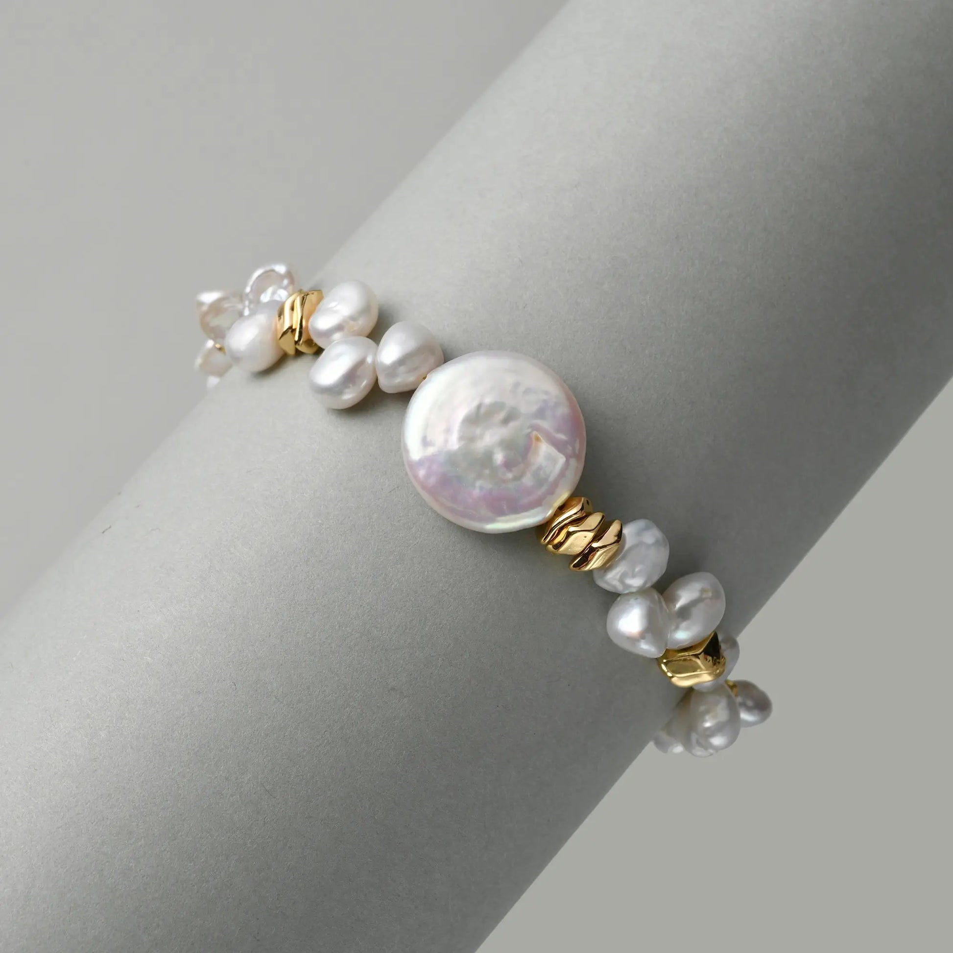 Top-down clean white close-up highlighting texture contrast between oversized luminous coin button baroque pearl, mini keshi pearls and sculptural twisted 18k gold metal beads