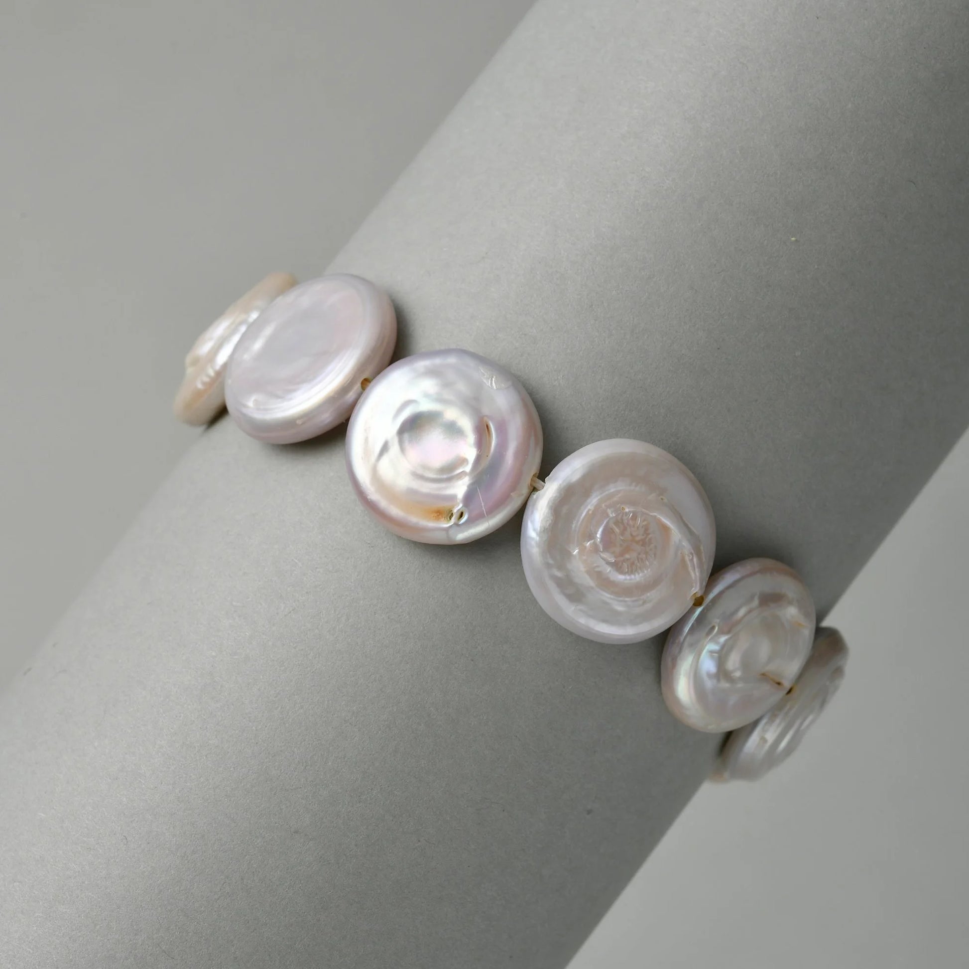 Neutral grey close-up highlighting soft shifting iridescent luster and subtle natural edge irregularities of flat coin-shaped white button baroque freshwater pearls