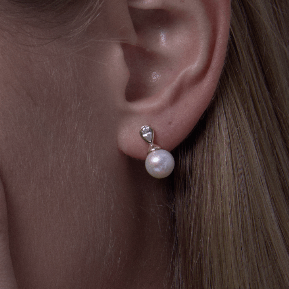 Solace pearl drop earrings worn on ear (lifestyle shot)