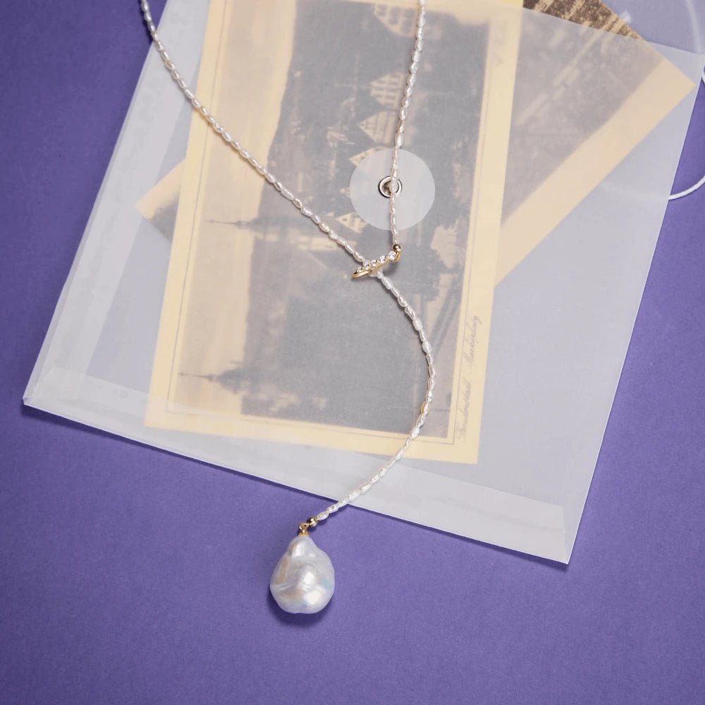 Soft neutral close-up highlighting texture contrast between tiny smooth oval rice pearls, luminous sculptural baroque pearl and twisted sparkling 18k gold Y-knot hardware