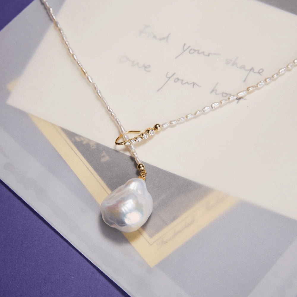 Top-down minimal white flat lay of full adjustable Y-lariat pearl necklace, complete oval rice pearl strand and large baroque drop pendant fully visible