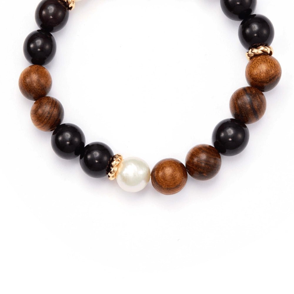 Minimal white close-up highlighting texture contrast between luminous smooth oval white pearls, grainy sandalwood & huanghuali hardwood beads and subtle polished brass metal spacers