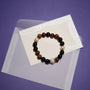 Soft lifestyle flat lay shot of wood oval pearl stretch bracelet laid on cream textured paper inside branded navy gift box, neutral earth tone minimalist styling
