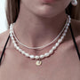 Medium close-up of neutral model wearing delicate tiny keshi pearl thin necklace, styled with minimal everyday outfit against soft neutral background.