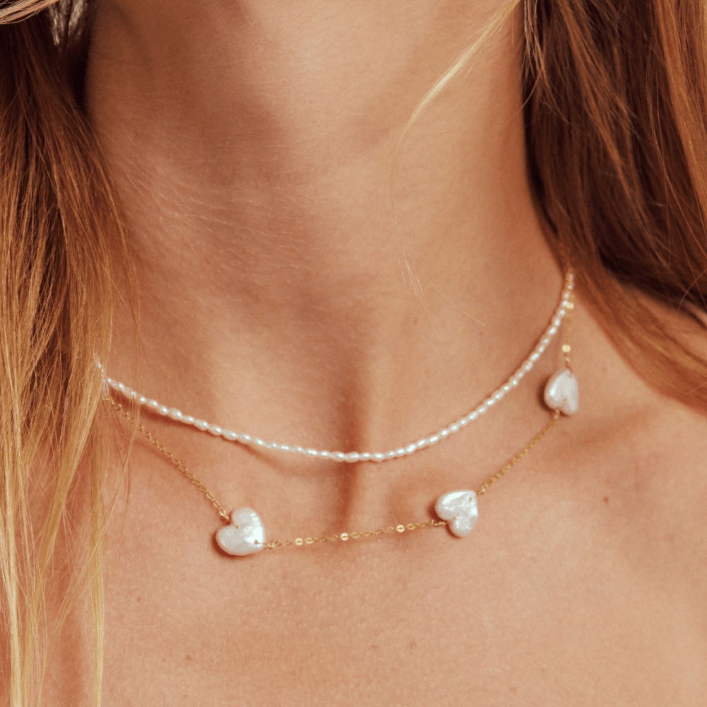 A layered necklace look featuring a heart on chain and baroque pearl necklace, perfect for a Coachella vibe or date night look.