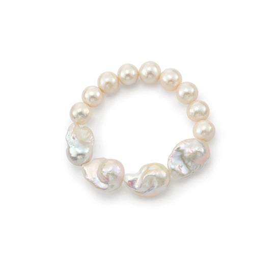 Top-down close-up of sterling silver stretch bracelet, round smooth pearls mixed with large organic white baroque focal pearls on plain white backdrop
