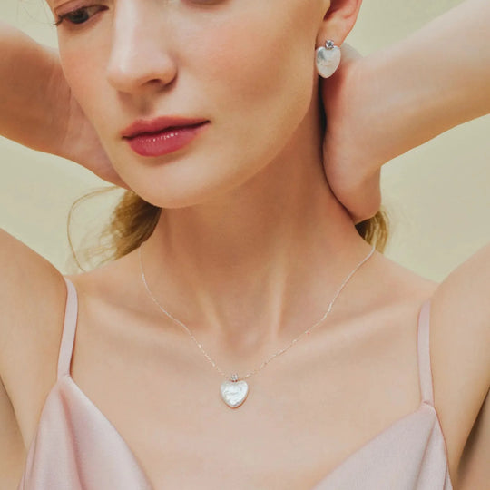 Soft close-up of young woman wearing heart baroque pearl drop earrings and matching sterling silver heart baroque pearl pendant  on neutral warm backdrop