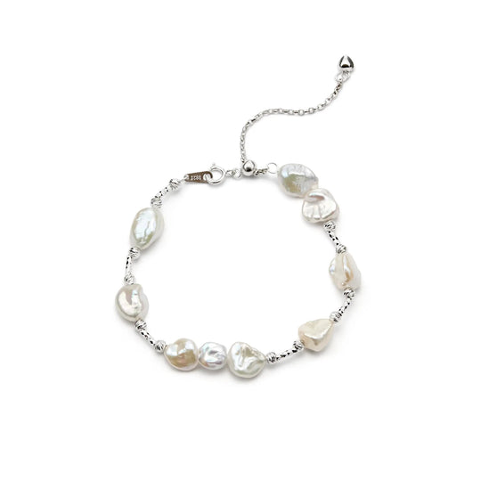 product shot of thin sterling silver bracelet strung with natural mini irregular white keshi pearls, fitted with lobster clasp and adjustable extender chain on white background